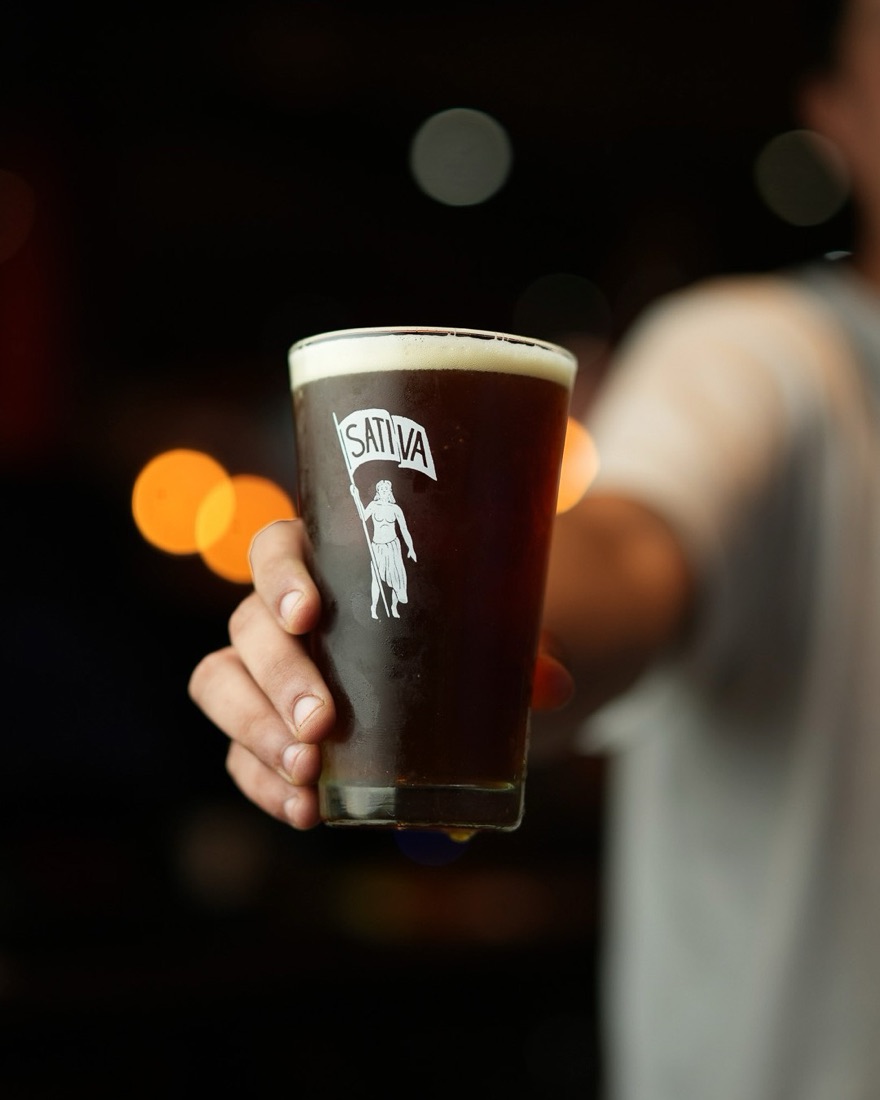 Mano que ofrece una pinta de cerveza artesanal oscura con espuma