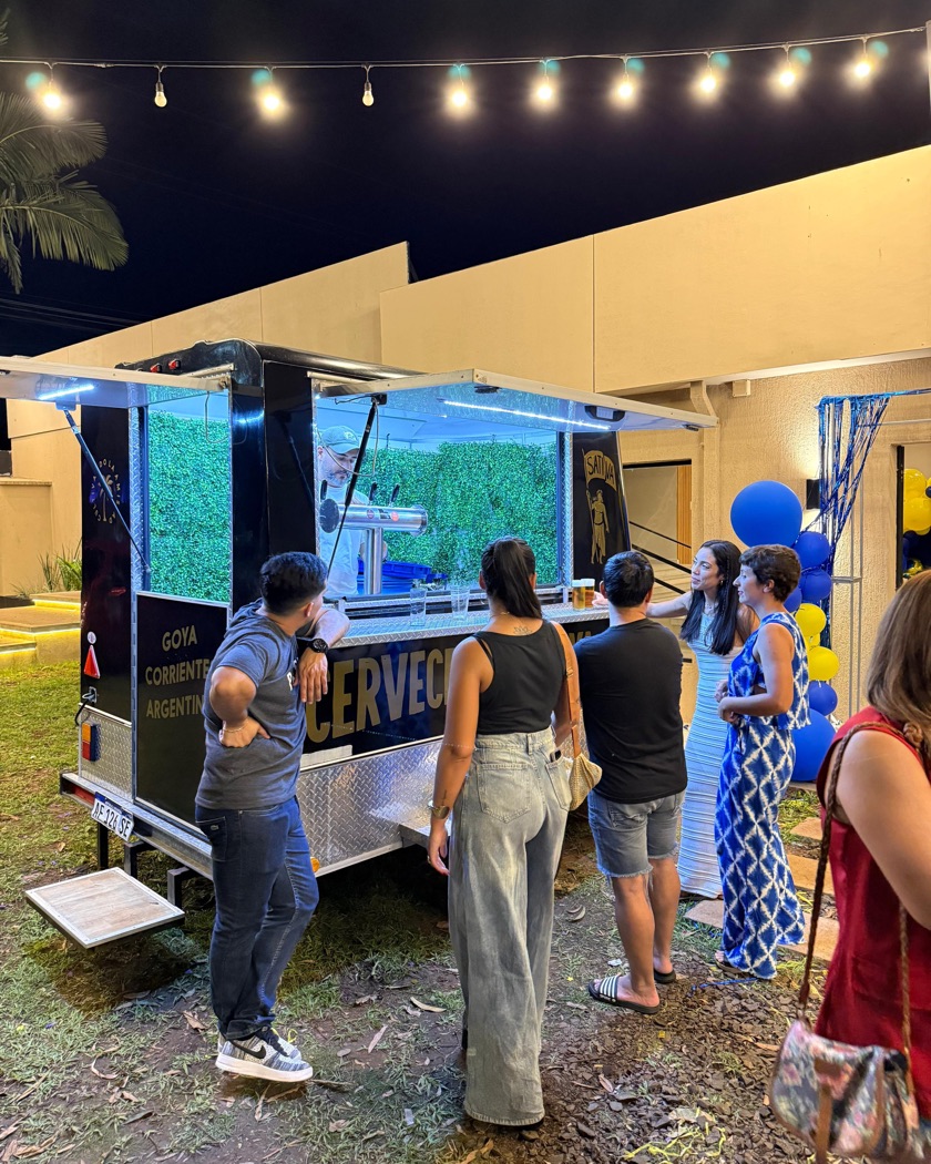 Invitados de un cumpleaños alrededor del stand de cerveza, de noche, con guirnaldas de luces