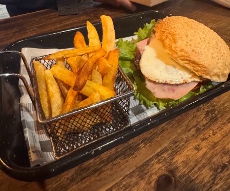 Hamburguesa con jamón, huevo frito y lechuga, con una canasta de papas fritas