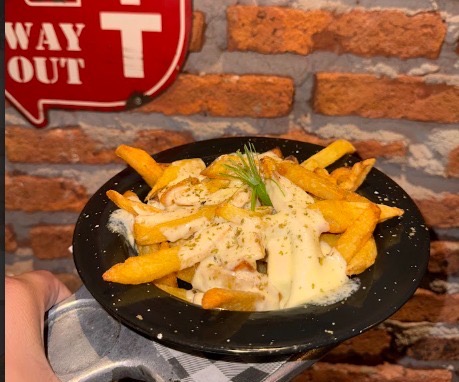 Plato de papas fritas gratinadas con queso derretido y orégano